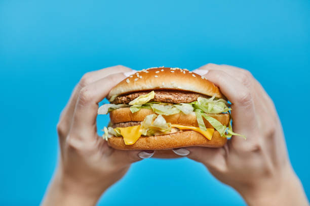 istock Woman hands holding a burger on a blue background 1189741388