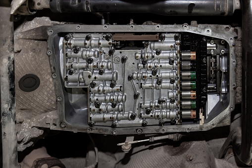 Bottom view of the bottom of the car with the transmission pan removed and a view of the solenoids lubricated with oil during repair and maintenance in the workshop for vehicles.