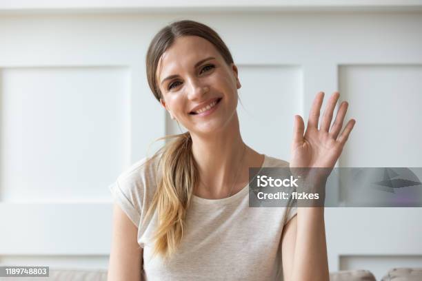 Gelukkige Aangename Jonge Vrouw Die Naar De Camera Kijkt Die Hallo Zwaaiende Stockfoto en meer beelden van Mensen