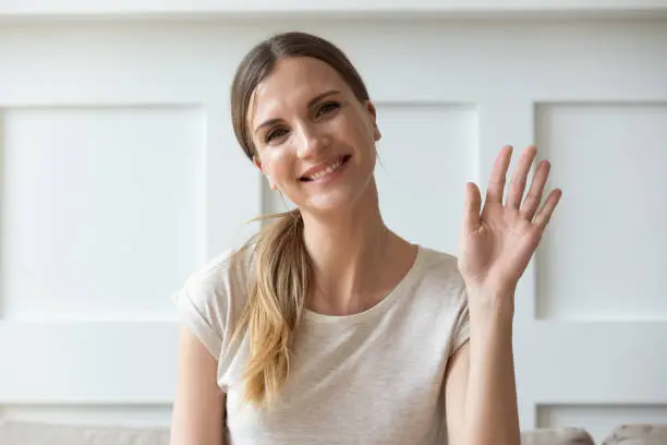 Photo of Happy pleasant young woman looking at camera, waving hello.