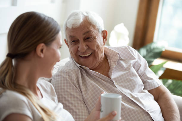 Happy old man talking with smiling grown up adult daughter. Head shot focus on happy old man talking with smiling grown up adult daughter, sitting together on sofa at home. Pleasant young woman communicating, having fun, laughing with retired 80s father. father daughter 80s stock pictures, royalty-free photos & images