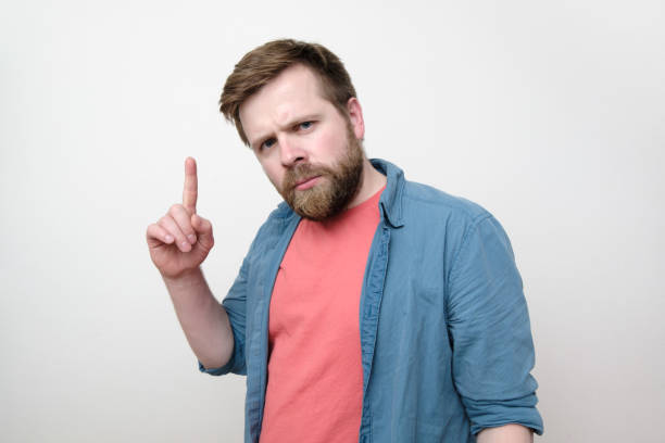 istock A serious, concerned man looks into the camera and points his finger upward, recalling the deadline. Isolated on white background. 1189754246