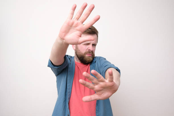 istock A calm, confident man put his palms forward as protection and narrowed one eye. Isolated on white background. 1189755123