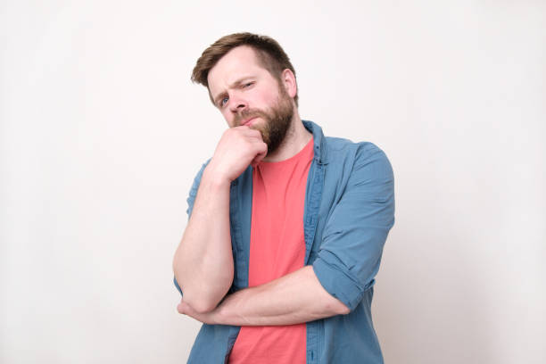istock A young bearded skeptical man looks into the camera. An expression of mistrust and suspicion. Isolated on white background. 1189755139