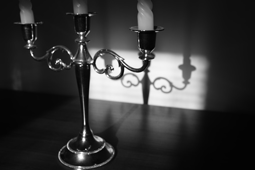Vintage candlestick on three candles with shadow reflection on the wall. Black and white photo