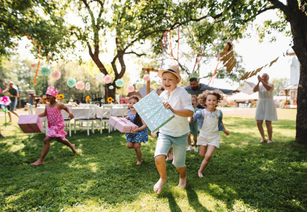 niños pequeños ruunning con el presente al aire libre en el jardín en la fiesta de cumpleaños. - birthday party fotografías e imágenes de stock