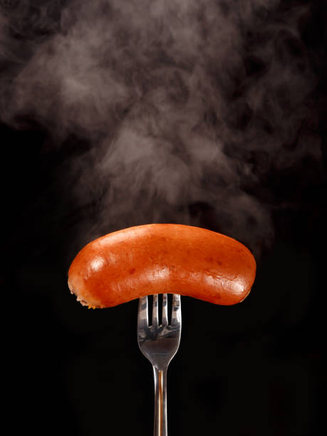 istock Hot boiled sausage with steam on a fork. Black background, close up 1189762737