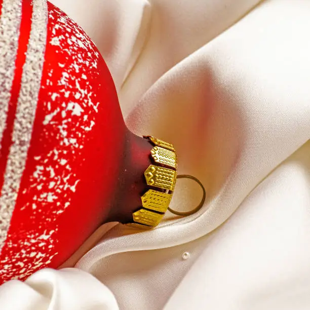 Photo of Red shiny christmas toy lies on a white silk cloth.. Christmas decorations and a red ribbon bow isolated on white. Hanging balls, star and snowflakes.