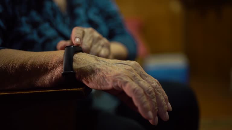 Old woman looks at the results of physical activity using a wristband fitness tracker at home