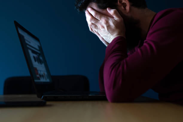 zestresowany młody człowiek pracuje późno na laptopie, czując się sfrustrowany i przygnębiony zakrywając twarz rękami późnym wieczorem - addiction internet computer working late zdjęcia i obrazy z banku zdjęć
