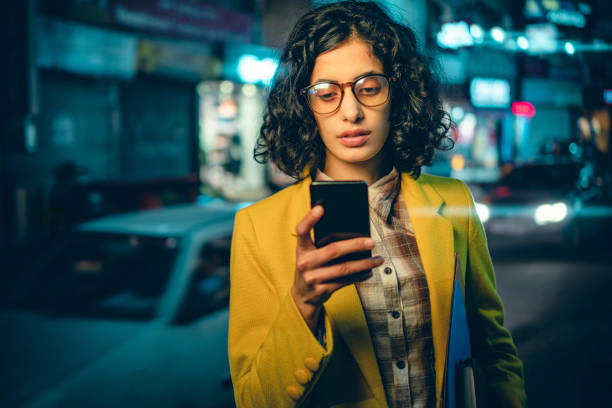 young adult businesswoman reads a smartphone on a busy road at night. - india car people business imagens e fotografias de stock