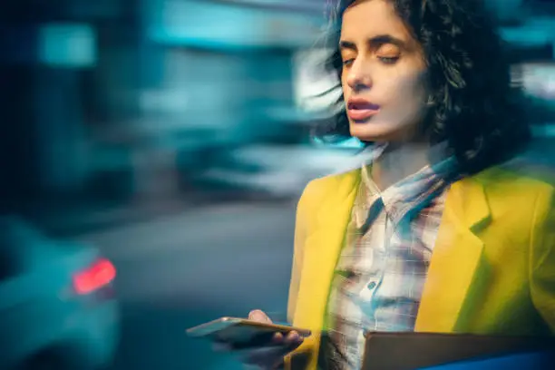 Photo of Young adult businesswoman after heavy use of smartphone feels dizzy at night on a busy road.