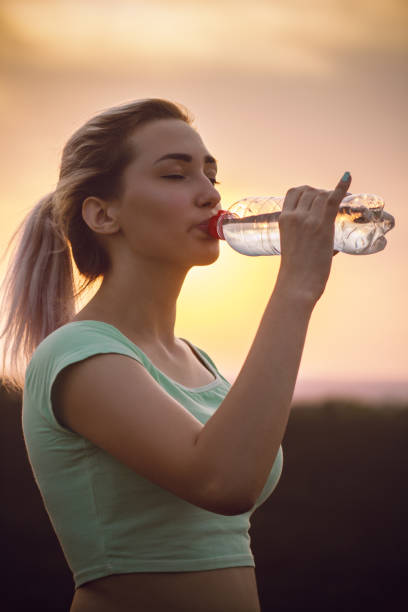 profilo silhouette di una bella ragazza che beve acqua dopo aver corso a distanza in un campo al tramonto, donna atletica con bottiglia all'aperto concetto sport e stile di vita sano - track and field athlete women vitality speed foto e immagini stock