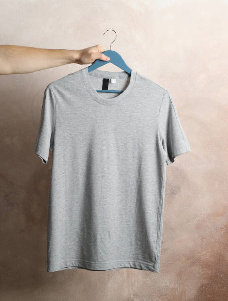 istock Man holds a hanger with blank gray t-shirt on brown background, space for text 1189776693