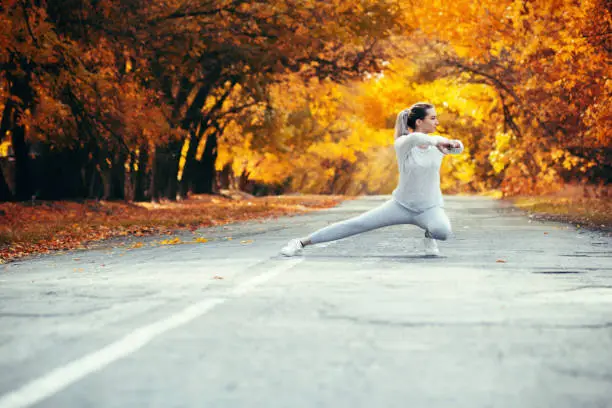 slim young woman in sportswear exercises and stretches on asphalt road, girl engaged in sport outdoors on background of autumnnature, concept healthy lifestyle
