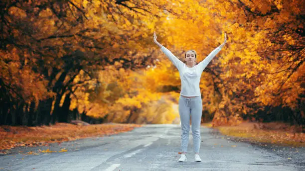slim young woman in sportswear exercises and stretches on asphalt road, girl engaged in sport outdoors on background of autumnnature, concept healthy lifestyle
