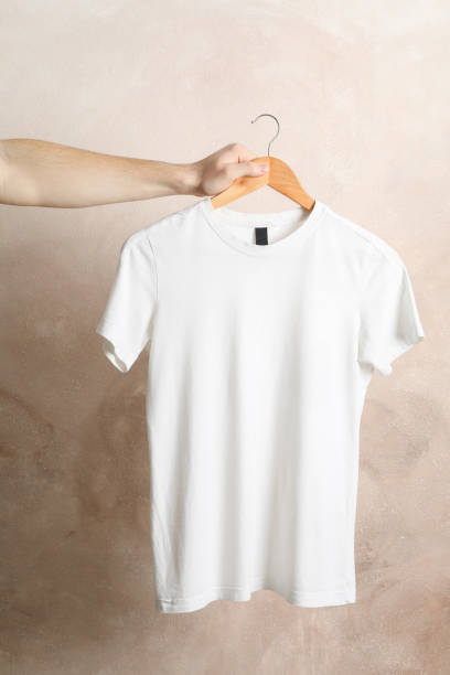 istock Man holds a hanger with blank white t-shirt on brown background, space for text 1189777079