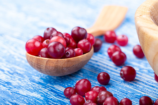 raw cranberries on a wooden table in a simple wooden spoon