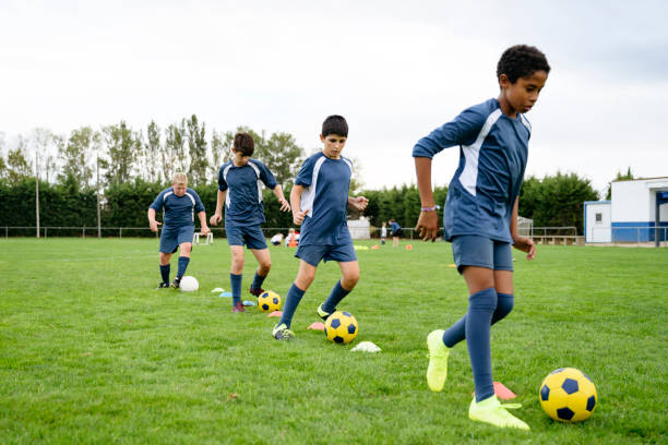 Young male footballers doing dribbling drills on field Group of focused young male footballers in blue jerseys practicing dribbling in sports training drill. bouncing photos stock pictures, royalty-free photos & images