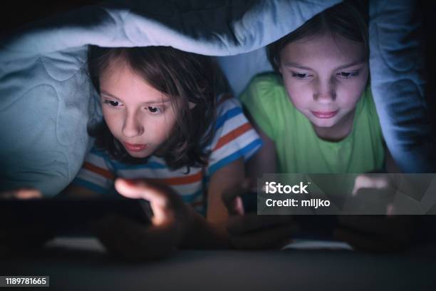 Boy And Girl Playing Games On Mobile Phone In Their Bed Stock Photo - Download Image Now