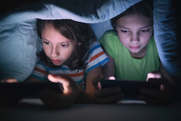 menino e menina que jogam jogos no telefone móvel em sua cama - video game child playing leisure games - fotografias e filmes do acervo