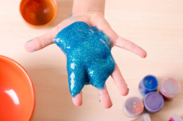 Photo of Child's hand holding bright glitter slime. Kid playing with slime, worldwide popular self made toy.