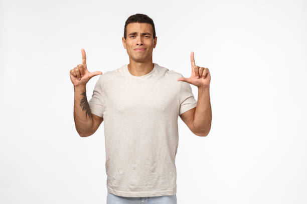 istock Indecisive and skeptical good-looking hispanic guy in white t-shirt, squinting and smirk from dislike, pointing up unsure, having concerns or doubts about personal choice, standing studio background 1189790557