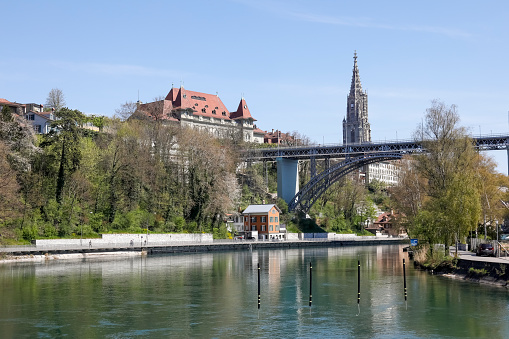 Bern, Switzerland - April 18, 2019: The river Aare flows under the bridge. In the area there are famous historic buildings and the cathedral tower is visible. The City of Bern is one of the countless great places in Switzerland and it is the political centre of this Country. Numerous museums, a wide cultural offer, a variety of tourist attractions makes it a travel destination for tourists from all over the world.
