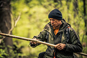 Survivalist man sharpening a stick in a forest
