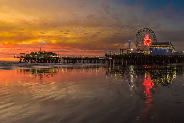 santa monica pier with orange sunset over and red heart displayed on ferris wheel. beautiful reflection of scene in the pacific ocean water. - santa monica city of los angeles los angeles county santa monica pier imagens e fotografias de stock