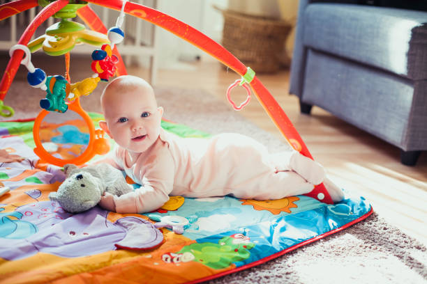 bambina di 4 mesi sdraiata su un colorato tappetino da gioco sul pavimento. tappeto di attività per bambini. - materassino foto e immagini stock