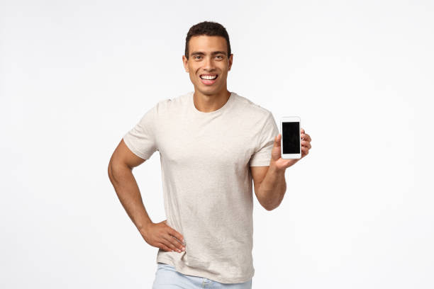 istock Proud and assertive handsome hispanic man in t-shirt, holding smartphone, promote application or shopping site, smiling delighted, give recommendation, advertise gadget or app, white background 1189792937