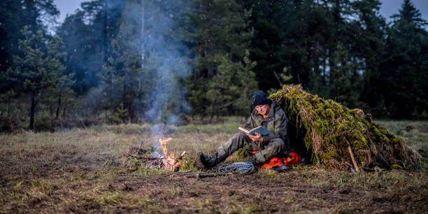 istock Man reading a book next to a campfire and makeshift shelter 1189793894