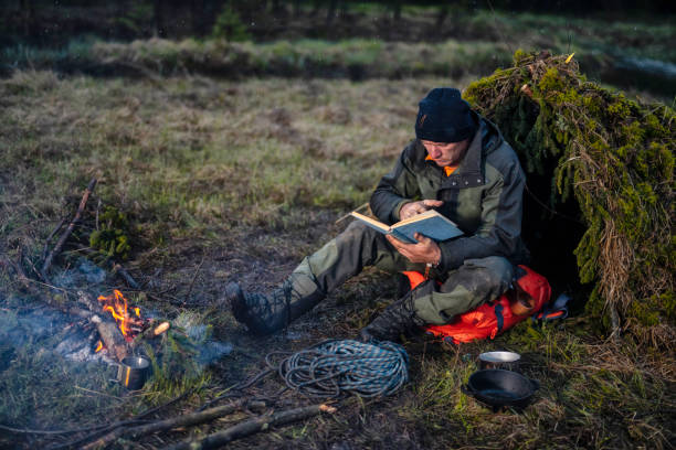 istock Man reading a book next to a campfire and makeshift shelter 1189793898