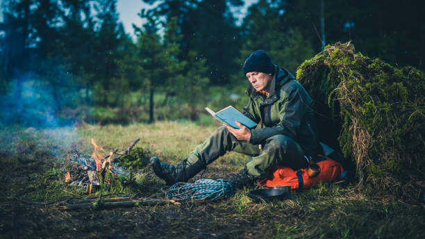 istock Man reading a book next to a campfire and makeshift shelter 1189793901