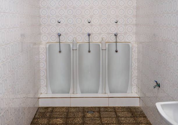 Set of three side by side full length mens urinals in porcelain against a tiled wall in small restroom