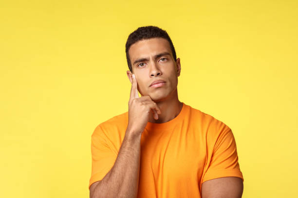 istock Pensive, serious-looking handsome guy in t-shirt look strict and thoughtful camera, touch temple as trying think, make-up plan, decide, have assumption, standing indecisive yellow background 1189796585