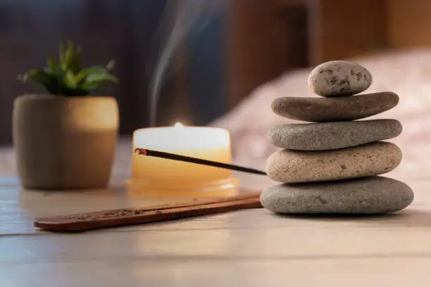Pyramid of zen stones, burning candle, incense stick, bedroom interior. Evening meditation concept. Close up.