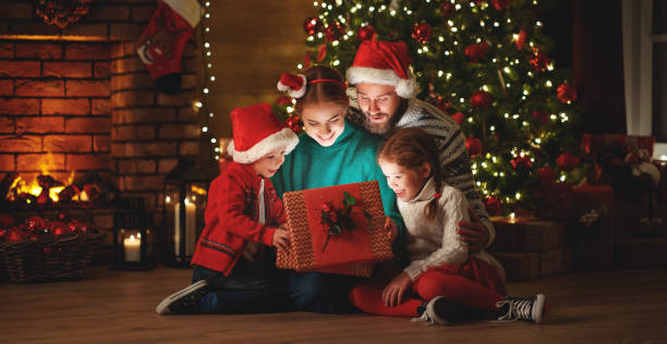 buon natale! felice famiglia madre padre e figli con regalo magico vicino albero a casa - christmas present immagine foto e immagini stock