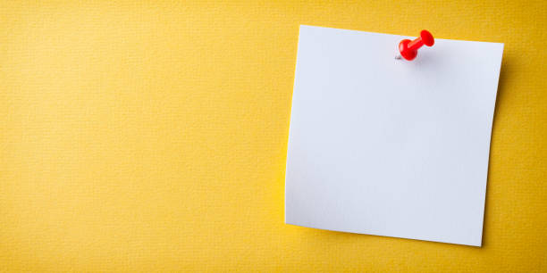 istock Blank white paper note pad reminder sticky notes on cork yellow background. Empty space for text. Office equipment. 1189804405