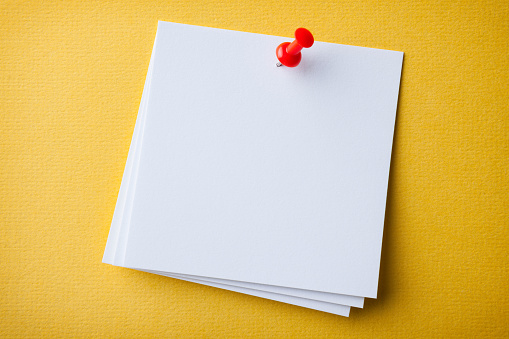 Blank white paper note pad reminder sticky notes on cork yellow background. Empty space for text. Office equipment.