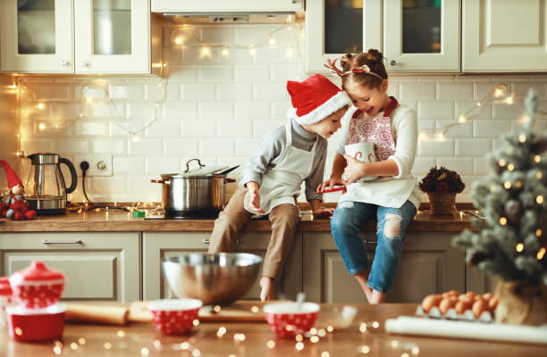 счастливые дети мальчик и девочка испечь рождественское печенье - santa hat фотографии стоковые фото и изображения