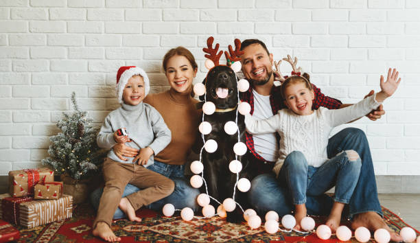 frohe weihnachten! familie mutter vater und kinder mit hund vor weihnachten mit girlande und baum - säugetier fotos stock-fotos und bilder