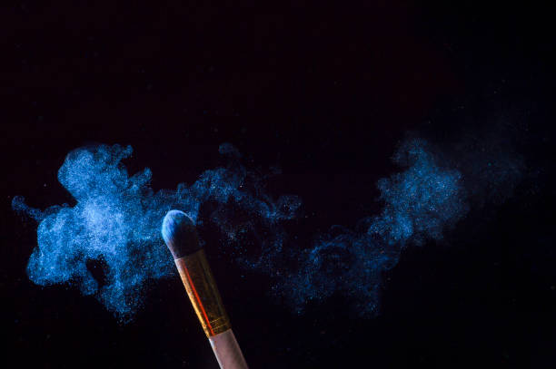 Make-up brush with blue powder explosion isolated on black background