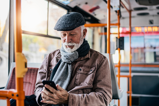 Smiling mature man with a long beard reading text messages on his cellphone while seated on a bus during his morning commute