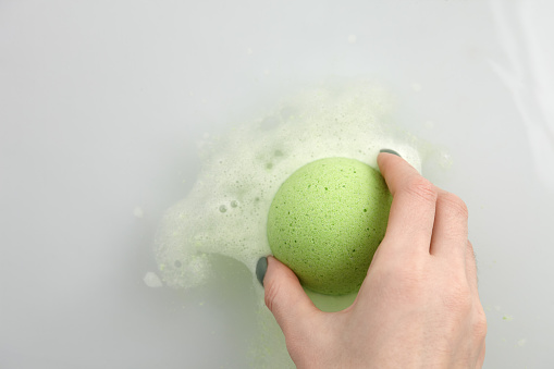 Woman's hand putting green bath bomb into water, copy space