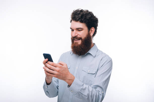 istock Young smiling hipster bearded man in casul using his phone over white background 1189814868