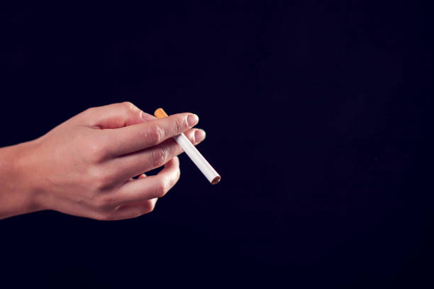 istock Cigarette in hand on black background. Nicotine addiction concept 1189814872