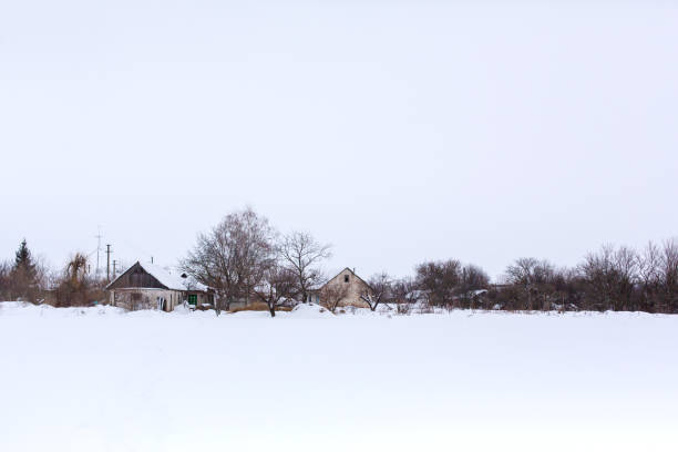 Typical Russian village among the winter forest. Lots of snow, sun and frost. Smoke rises from chimneys. View of the village from the car window. Russian landscape.
