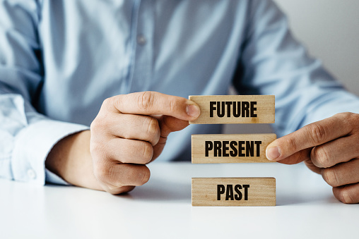 A businessman arranges wooden jigsaw blocks one on top of the other with the words past, present and future.